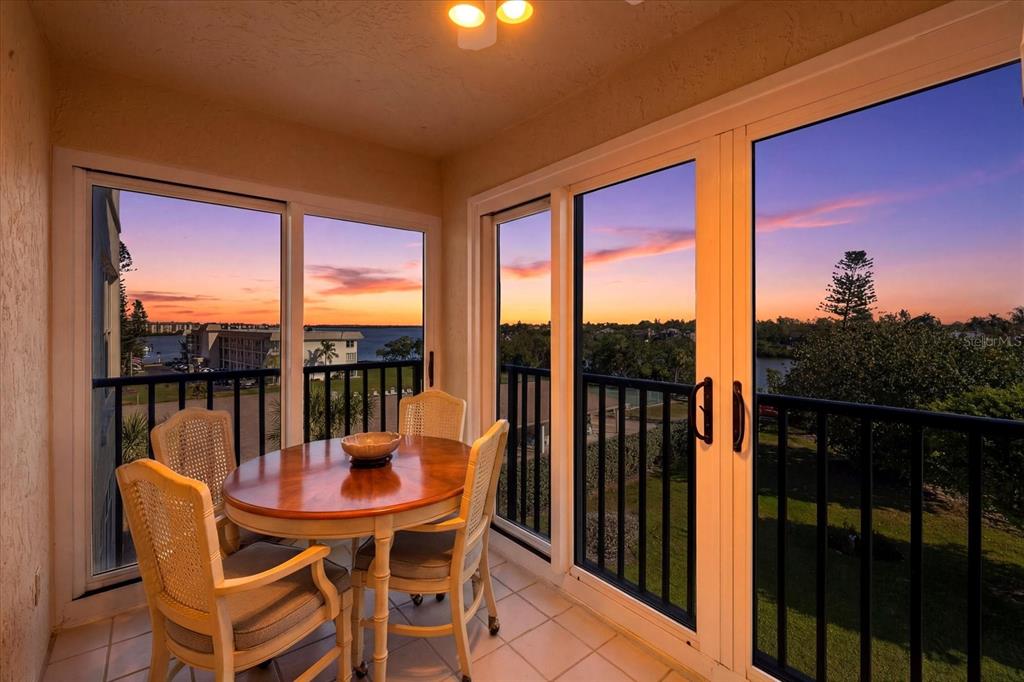 A sunroom with a dining table and chairs overlooks a waterfront view at sunset — 3240 GULF OF MEXICO DRIVE UNIT B402, LONGBOAT KEY, FL