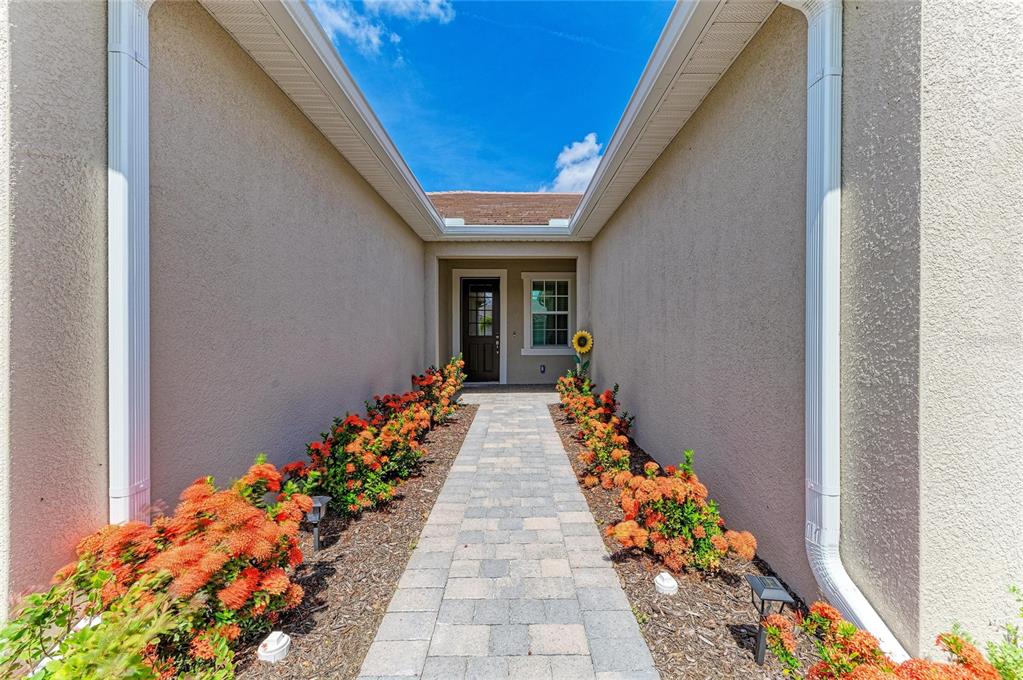 A paved walkway leads to the front door of a house flanked by orange flowering shrubs — 17827 STILLNESS COURT, VENICE, FL