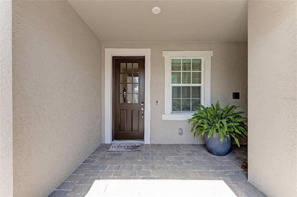 A covered entryway features a dark brown front door, a window, and a potted fern — 17827 STILLNESS COURT, VENICE, FL