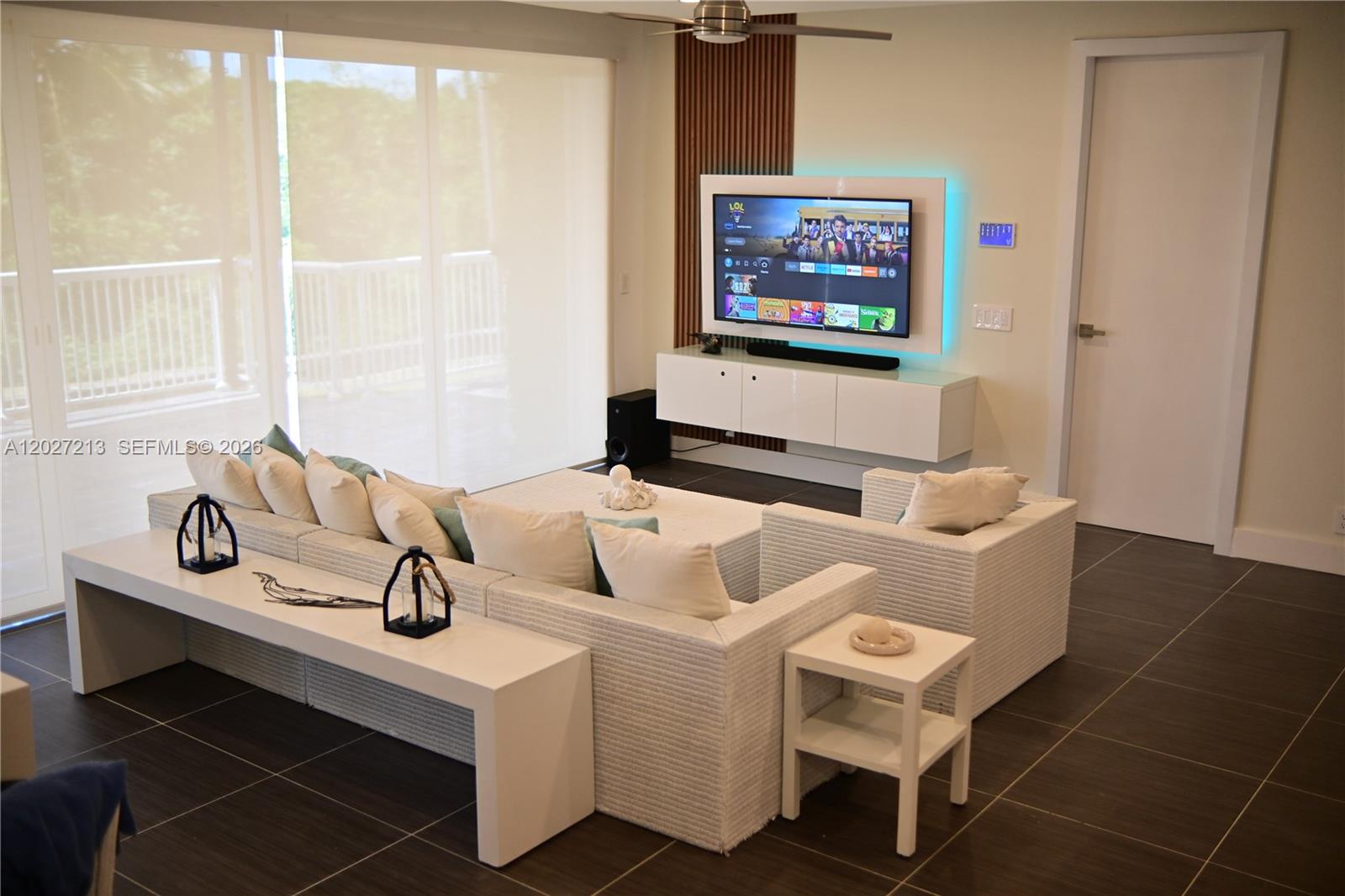 A modern living room features a white sectional sofa, a wall-mounted television, and tile flooring — Highway#5 Vista Mare # 102, FL 32000, FL