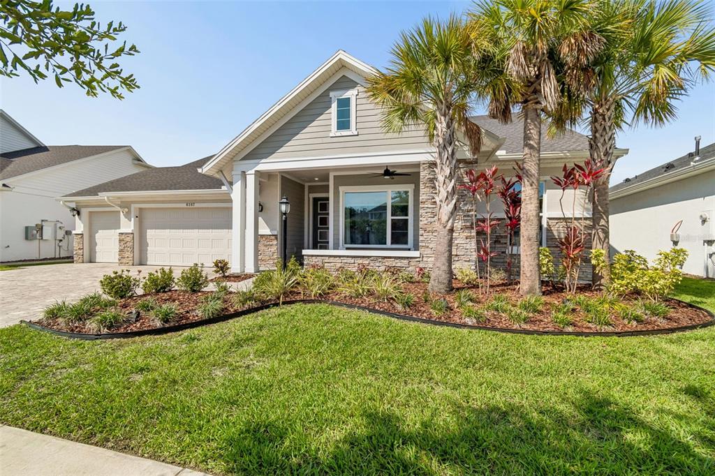 A single-story house with a stone facade, gray siding, a two-car garage, and palm trees — 6107 NIKKI LANE LANE, ODESSA, FL