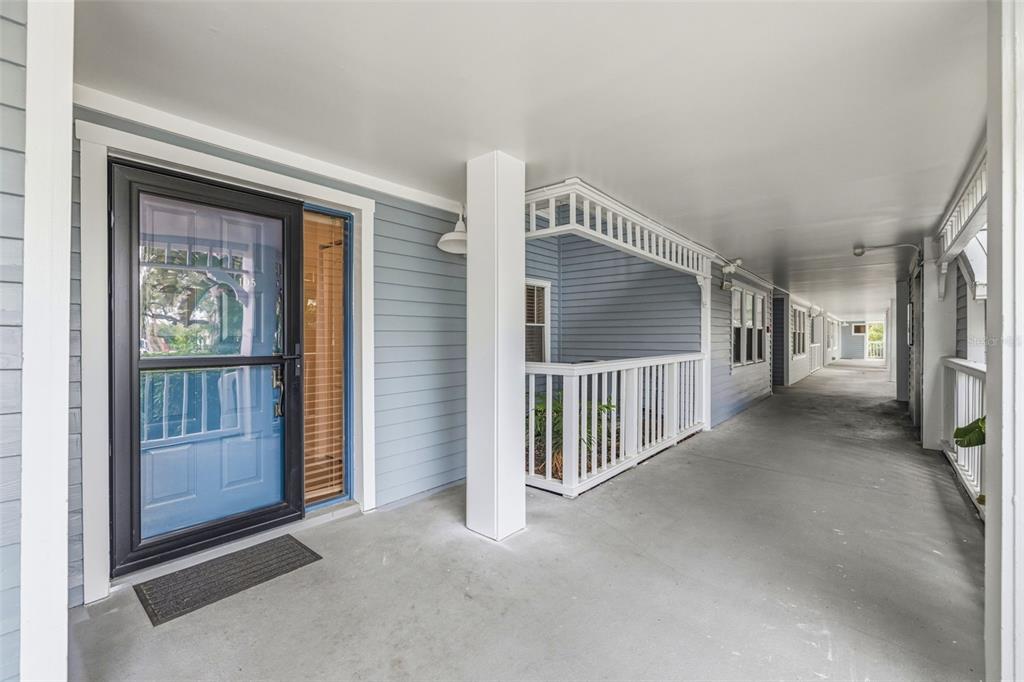 A covered walkway with blue siding leads to a front door with a storm door — 2533 DOLLY BAY DRIVE UNIT 105, PALM HARBOR, FL