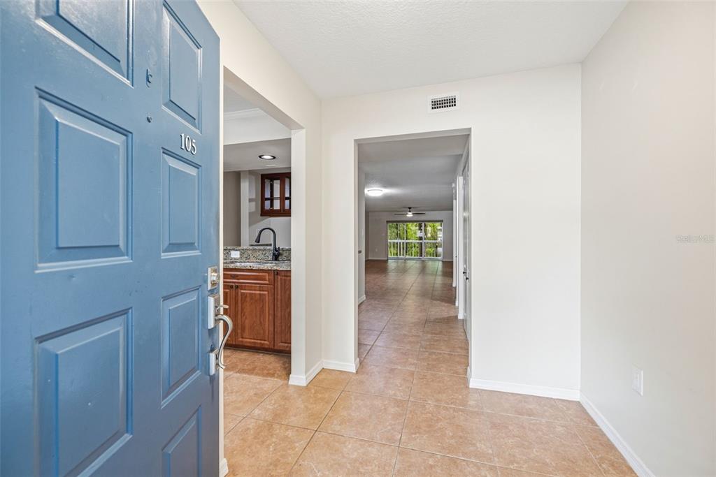 An entryway with a blue door opens into a tiled hallway leading to a living area — 2533 DOLLY BAY DRIVE UNIT 105, PALM HARBOR, FL