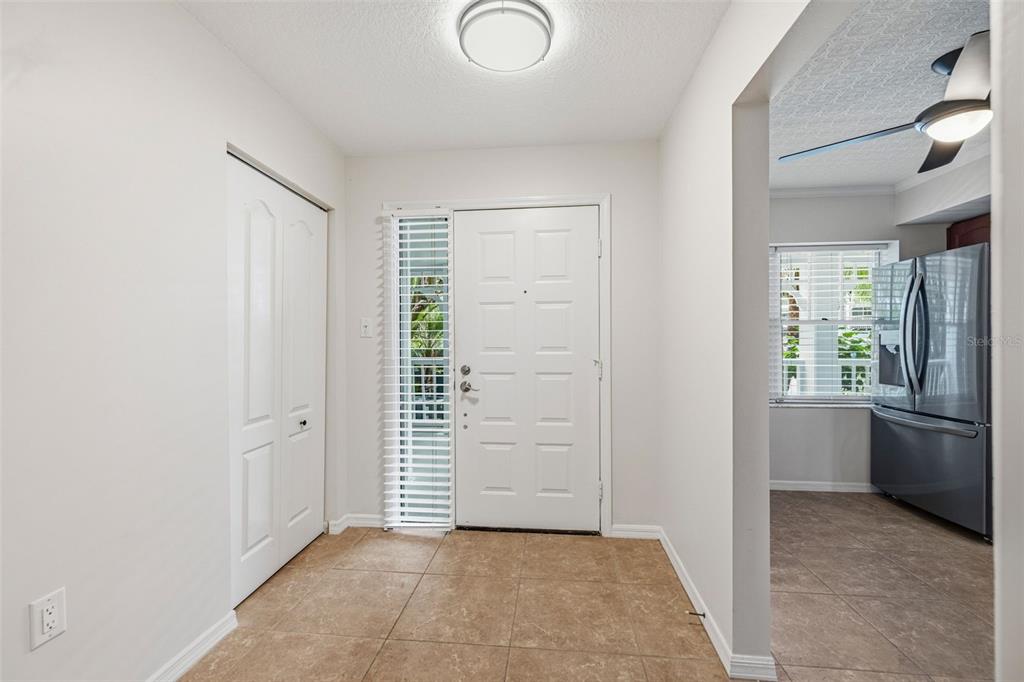 An entryway with tile flooring, a white front door, a closet, and a kitchen view — 2533 DOLLY BAY DRIVE UNIT 105, PALM HARBOR, FL