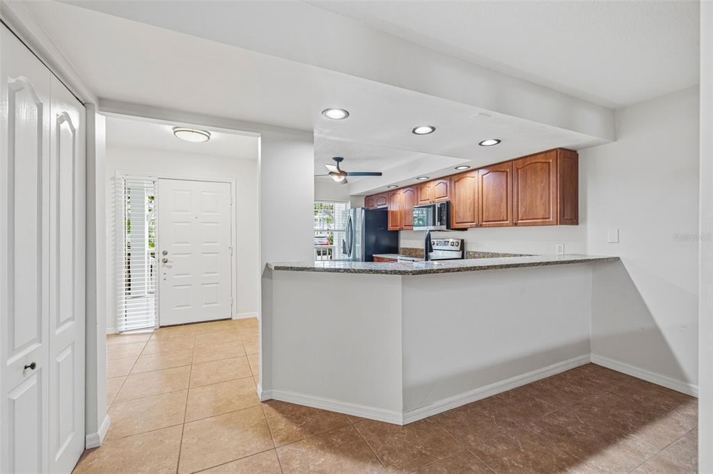 A kitchen with wood cabinets and granite countertops overlooks a tiled living area and entryway — 2533 DOLLY BAY DRIVE UNIT 105, PALM HARBOR, FL
