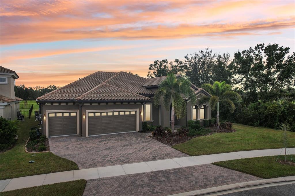 A single-story house with a tiled roof, three-car garage, and paved driveway at sunset — 14235 SWISS BRIDGE DRIVE, RIVERVIEW, FL