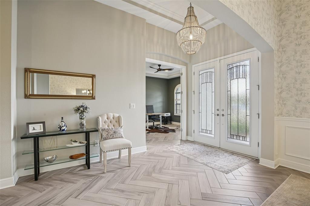 A bright foyer features herringbone tile flooring, a glass console table, and a beaded chandelier — 14235 SWISS BRIDGE DRIVE, RIVERVIEW, FL