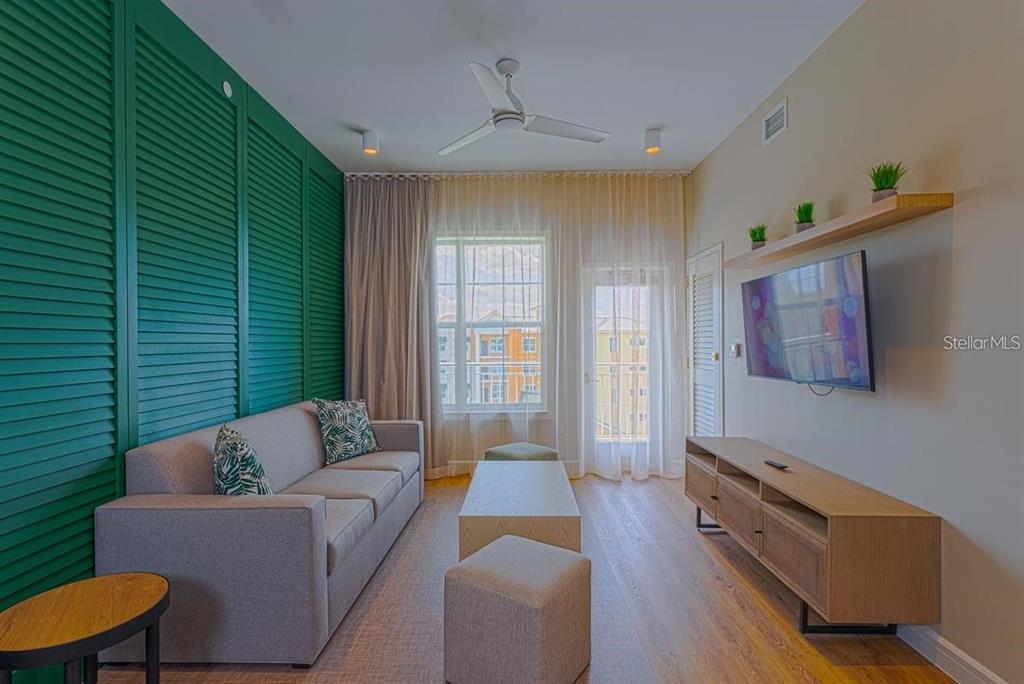 A living room features a green shuttered wall, a gray sofa, and a wall-mounted television — 3151 SUNSET WALK DRIVE UNIT 518, KISSIMMEE, FL