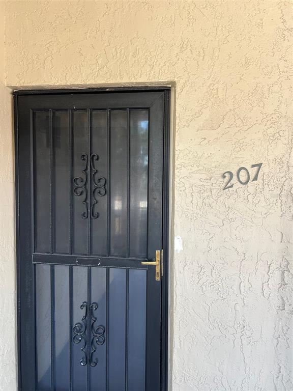 A black metal security screen door is mounted on a beige stucco exterior wall — 7951 58TH AVENUE N UNIT 207, ST PETERSBURG, FL