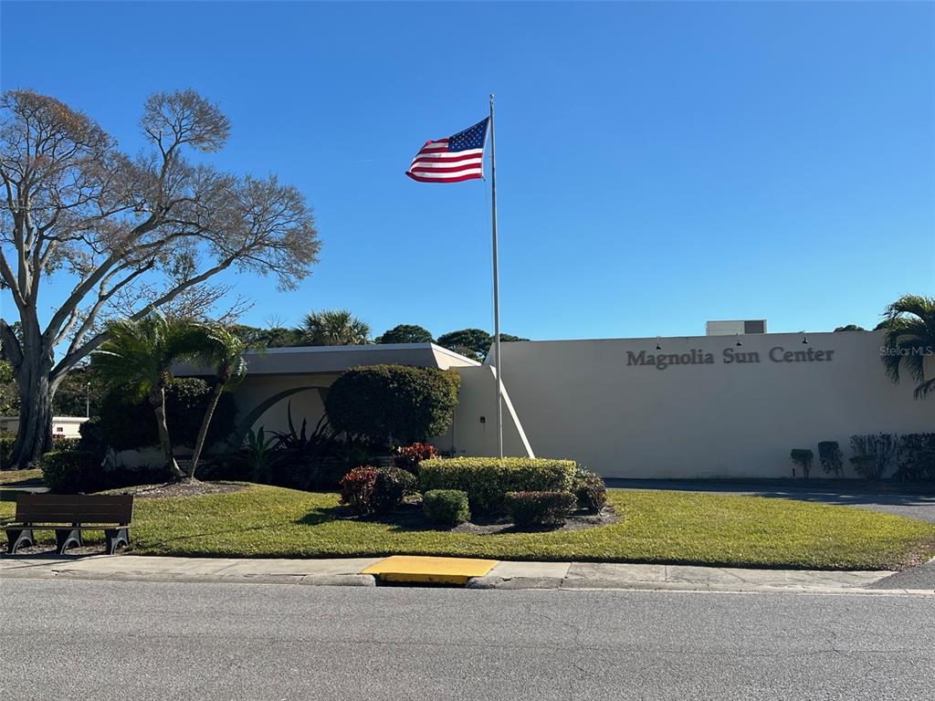 The exterior of the Magnolia Sun Center features a beige building, a flagpole, and landscaping — 7951 58TH AVENUE N UNIT 207, ST PETERSBURG, FL