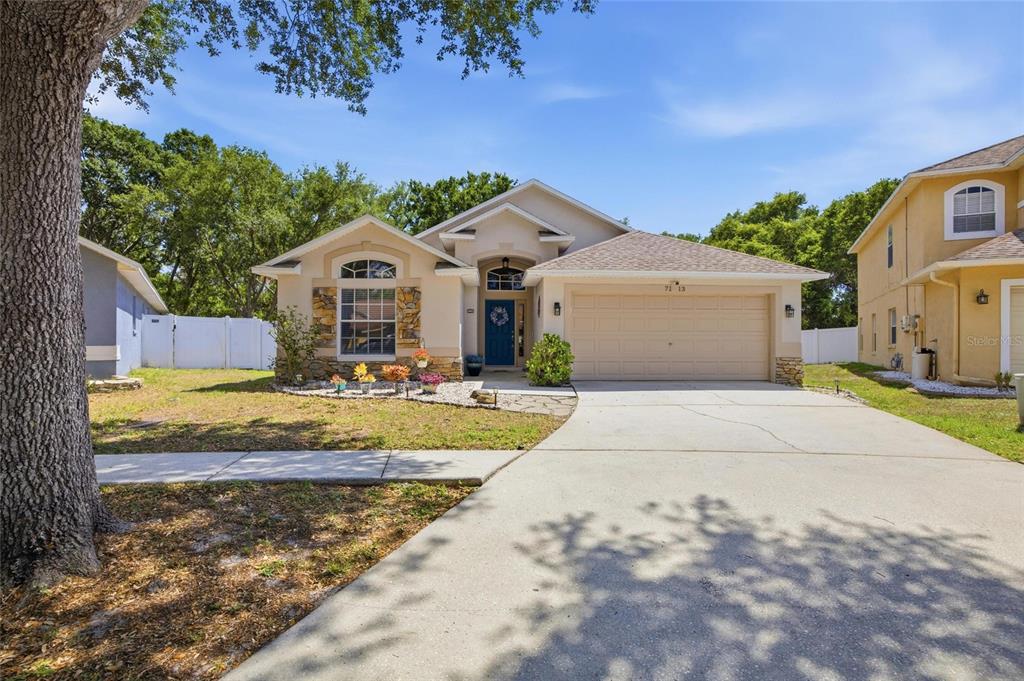 A single-story house with a beige stucco exterior, stone accents, and a two-car garage — 7113 COLONY POINTE DRIVE, RIVERVIEW, FL
