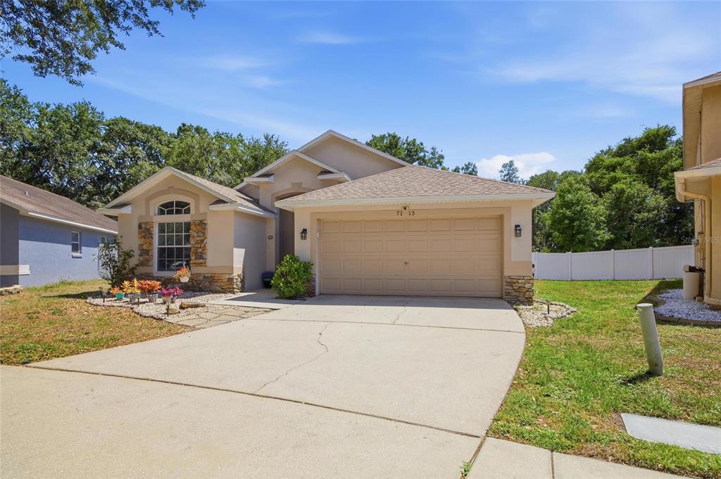 A single-story suburban house with a beige stucco exterior, stone accents, and a two-car garage — 7113 COLONY POINTE DRIVE, RIVERVIEW, FL
