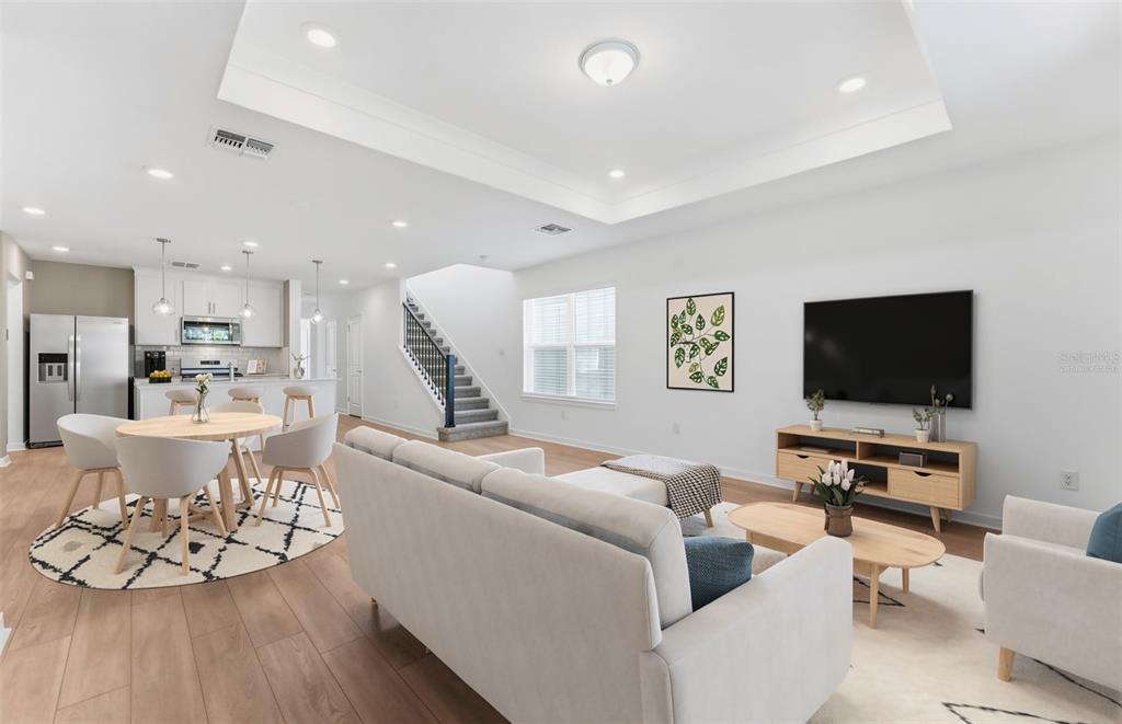 An open-concept living room and kitchen featuring light wood flooring, a staircase, and neutral furniture — 5344 SPRING MAIDEN CIRCLE, APOLLO BEACH, FL