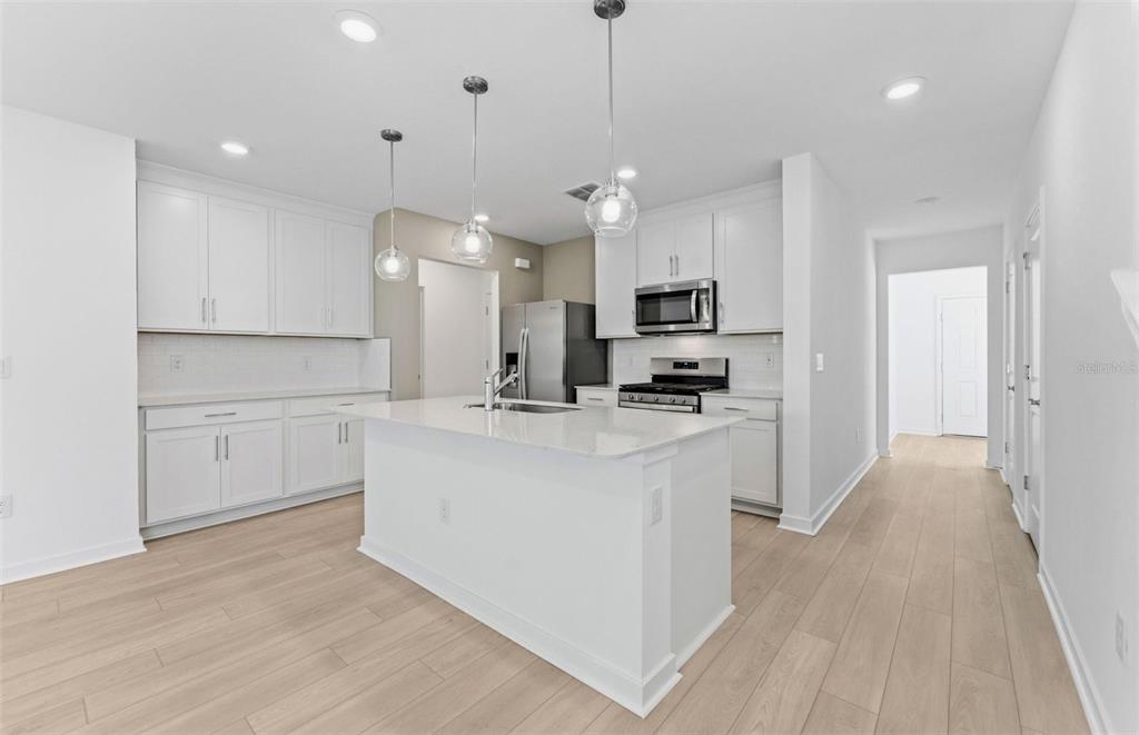 A modern kitchen features white cabinetry, a central island with a sink, and light flooring — 5344 SPRING MAIDEN CIRCLE, APOLLO BEACH, FL