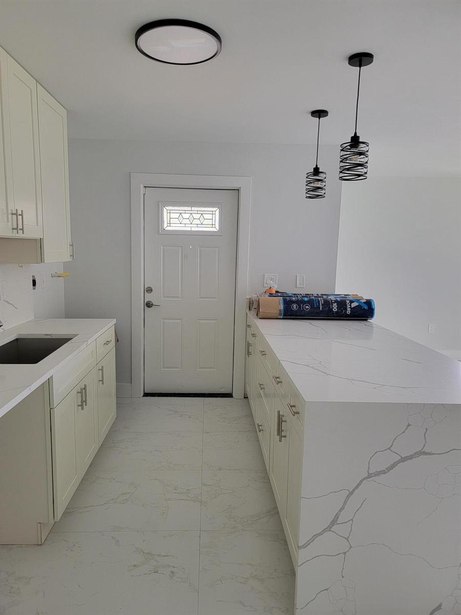 A kitchen features white cabinets, marble-patterned countertops, a large island, and light-colored tile flooring — 240 SW 7th Street # 9, Boca Raton FL 33432, BOCA RATON, FL