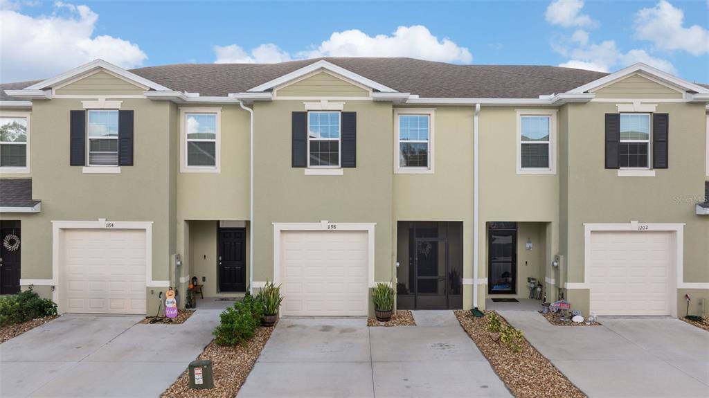 An exterior view of a multi-unit townhouse complex with beige stucco walls and garages — 1198 LIDO DRIVE, HOWEY IN THE HILLS, FL
