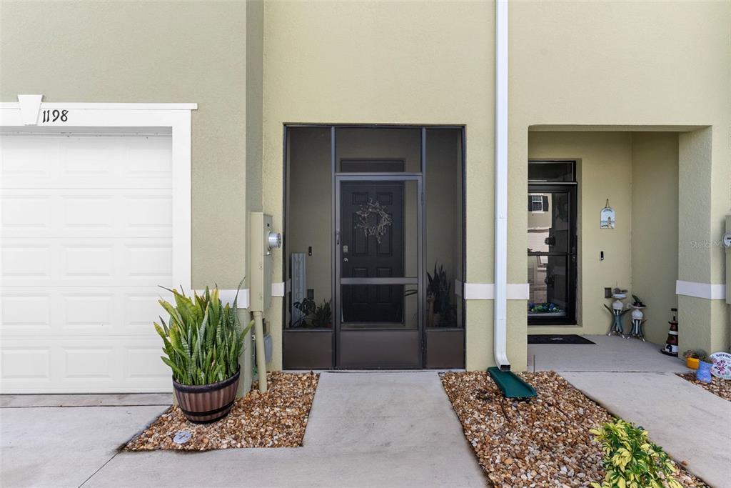 The exterior of a townhouse features a garage, a screened front entryway, and gravel landscaping — 1198 LIDO DRIVE, HOWEY IN THE HILLS, FL