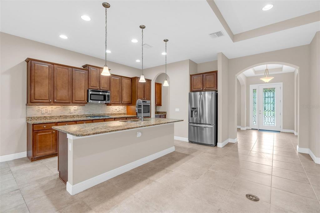 A kitchen with brown cabinets, granite countertops, a center island, and stainless steel appliances — 903 VICTORIA HILLS DRIVE S, DELAND, FL