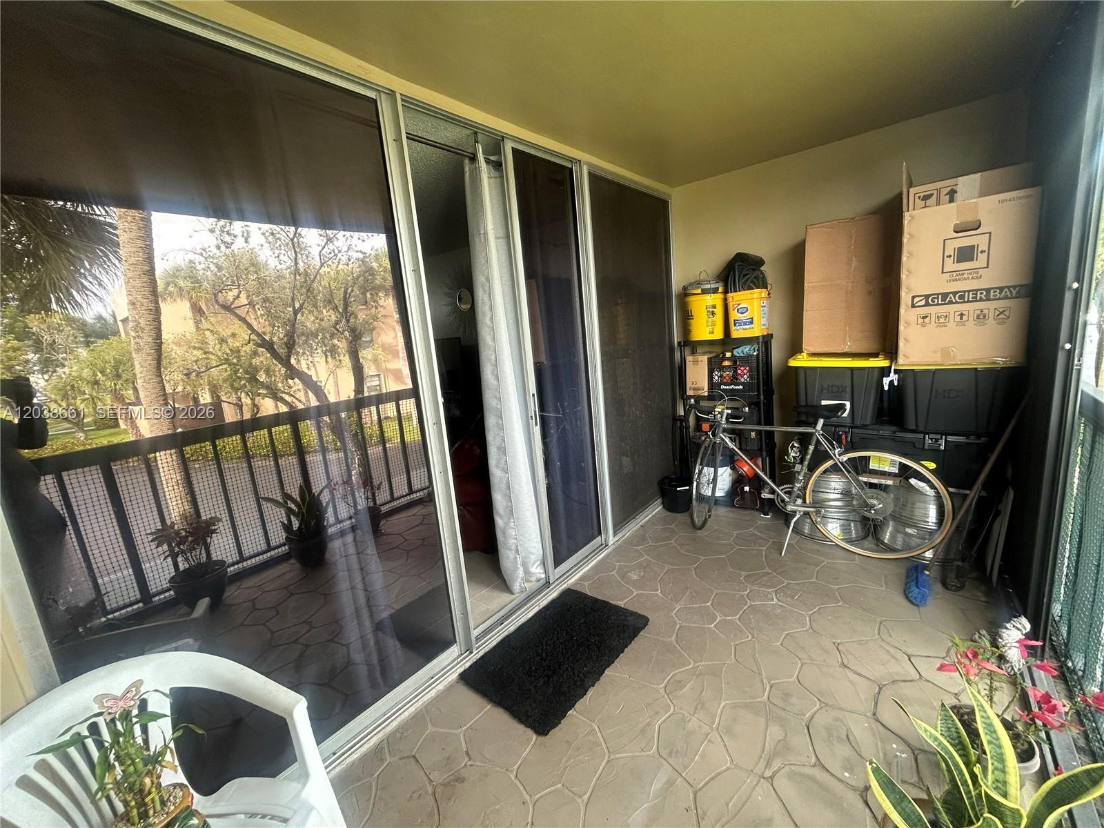 A covered balcony features a stone-patterned floor, sliding glass doors, and a bicycle with storage — 10875 SW 112th Ave # 203, Miami FL 33176, MIAMI, FL