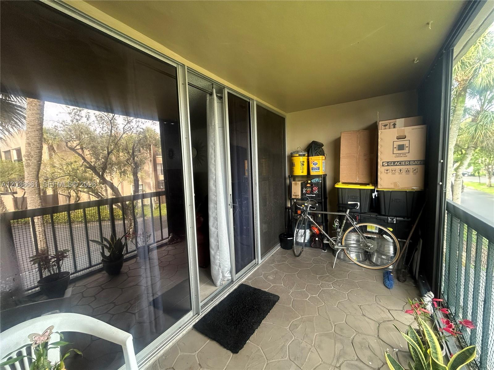 A covered balcony features stone-patterned flooring, sliding glass doors, a bicycle, and stacked storage boxes — 10875 SW 112th Ave # 203, Miami FL 33176, MIAMI, FL