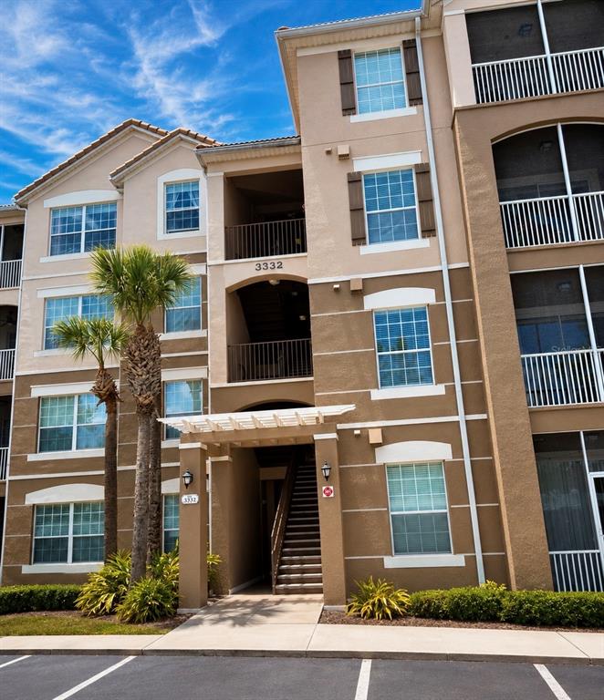 A multi-story apartment building exterior features tan stucco walls, brown shutters, and a covered entryway — 3332 ROBERT TRENT JONES DRIVE UNIT 20603, ORLANDO, FL