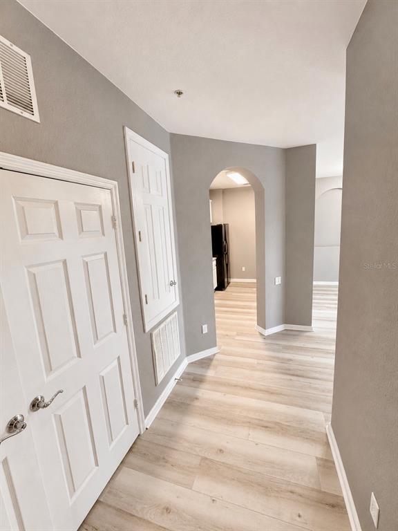 A hallway with light wood-look flooring leads through an arched doorway toward a kitchen area — 3332 ROBERT TRENT JONES DRIVE UNIT 20603, ORLANDO, FL