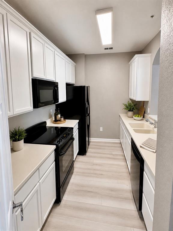 A galley kitchen features white cabinets, black appliances, light countertops, and light wood-look flooring — 3332 ROBERT TRENT JONES DRIVE UNIT 20603, ORLANDO, FL