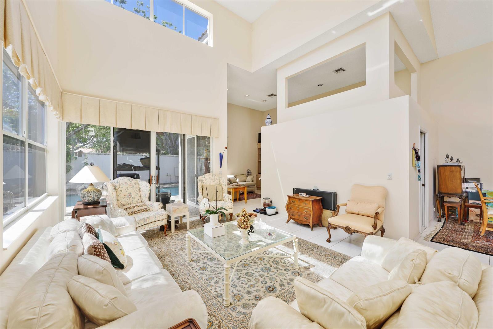 A bright, high-ceilinged living room features white sofas, a glass coffee table, and large windows — 2502 NW 66th Drive, Boca Raton FL 33496, BOCA RATON, FL