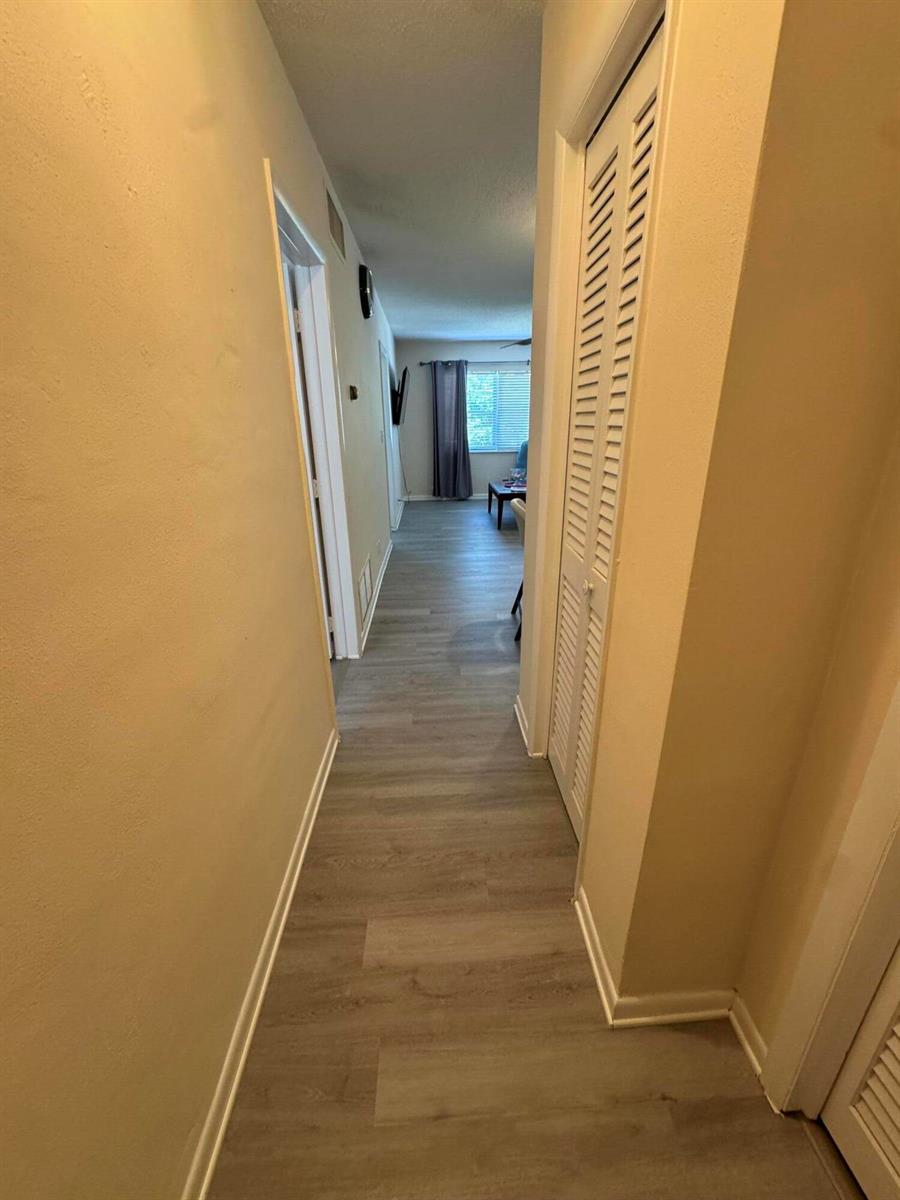 A hallway with light wood-look flooring leads toward a windowed living area — 2851 E Golf Boulevard # 206, Pompano Beach FL 33064, POMPANO BEACH, FL