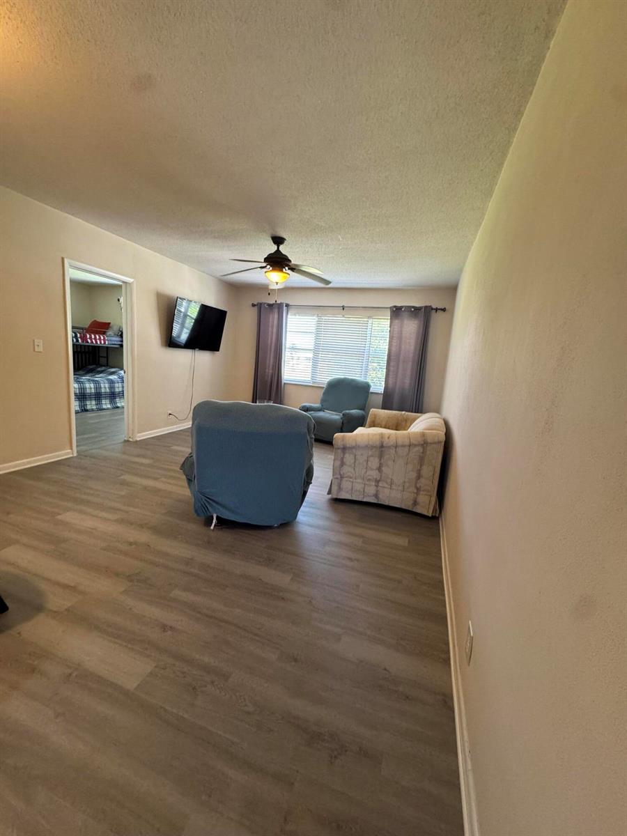 A living room with light wood-look flooring, a ceiling fan, and several pieces of furniture — 2851 E Golf Boulevard # 206, Pompano Beach FL 33064, POMPANO BEACH, FL