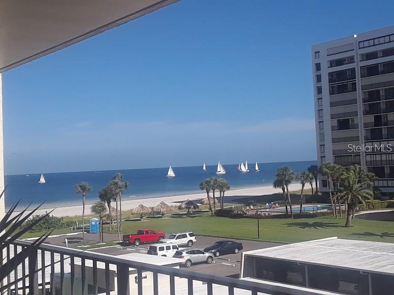 An elevated view of a beach, ocean with sailboats, parking lot, and a high-rise building — 1480 GULF BOULEVARD UNIT 309, CLEARWATER BEACH, FL