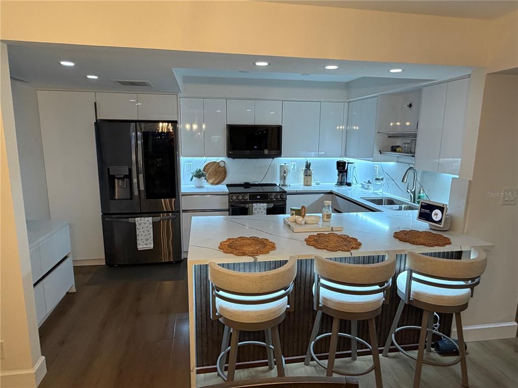 A modern kitchen features white cabinets, a marble-topped island with three stools, and stainless appliances — 1480 GULF BOULEVARD UNIT 309, CLEARWATER BEACH, FL