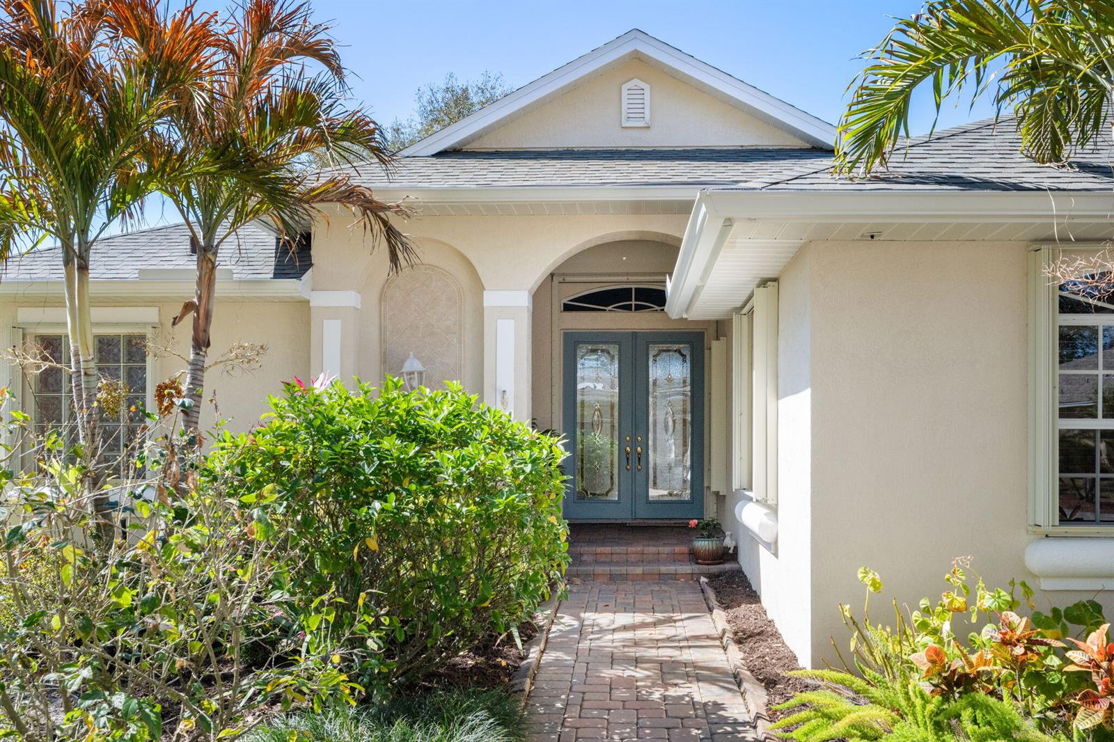 A front view of a house with a brick walkway leading to double glass doors — 4220 Abington Woods Circle, Vero Beach FL 32967, VERO BEACH, FL