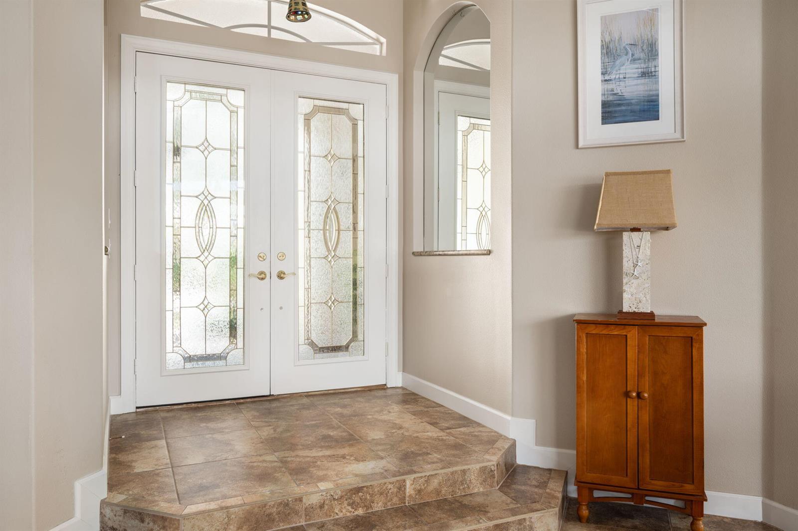 An entryway features double glass-paneled doors, a raised tiled landing, and a wooden cabinet — 4220 Abington Woods Circle, Vero Beach FL 32967, VERO BEACH, FL
