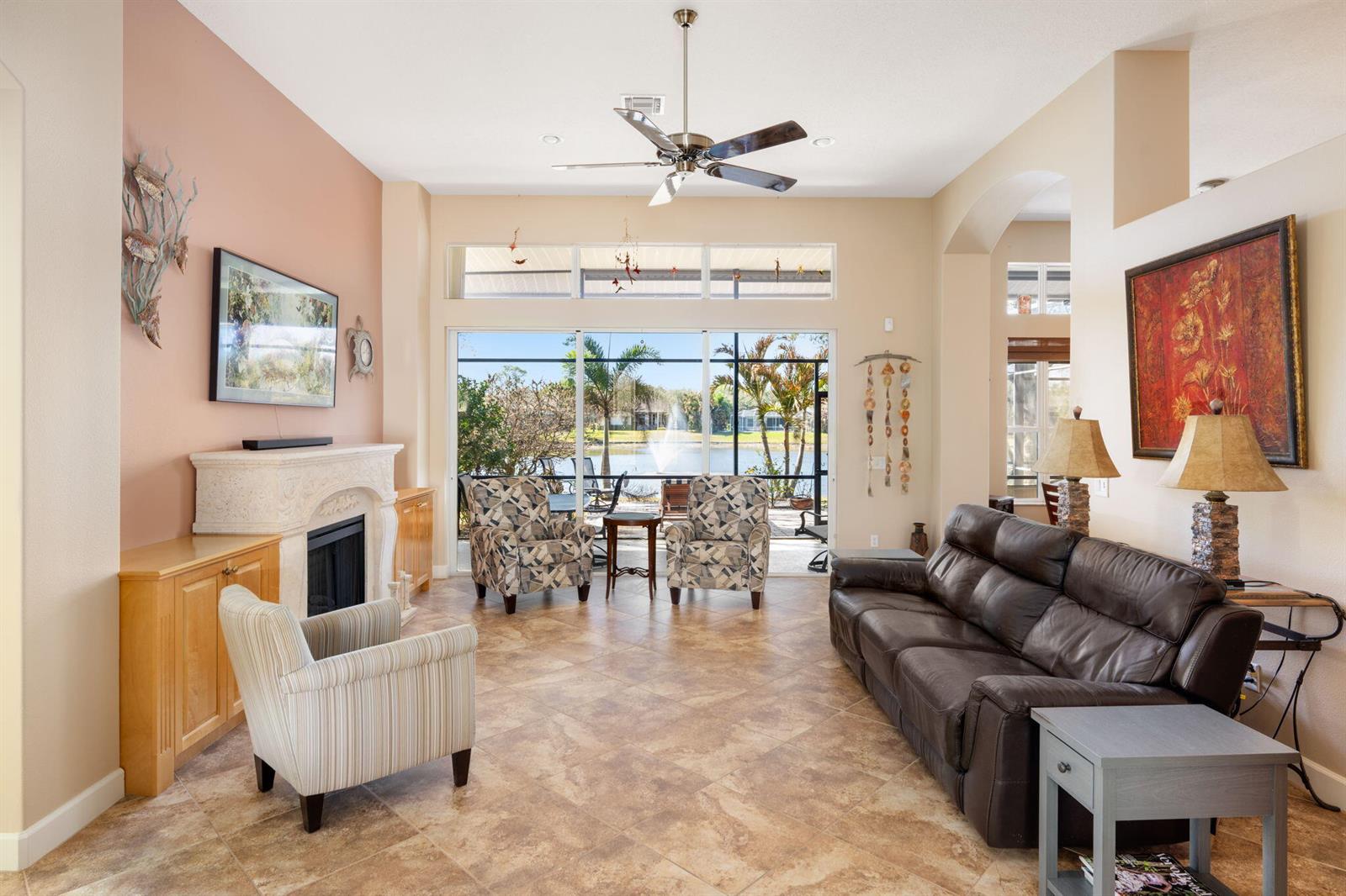 A living room features a fireplace, leather sofa, tiled floors, and sliding doors to a lake — 4220 Abington Woods Circle, Vero Beach FL 32967, VERO BEACH, FL