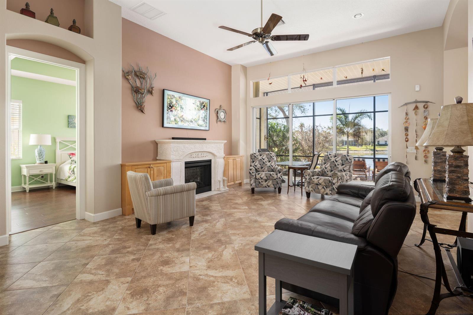 A living room with tile floors, a fireplace, and large windows overlooking a lake — 4220 Abington Woods Circle, Vero Beach FL 32967, VERO BEACH, FL