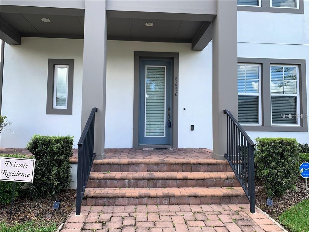 The front entrance features a blue door, brick steps, and black metal railings — 8650 TAVISTOCK LAKES BOULEVARD, ORLANDO, FL