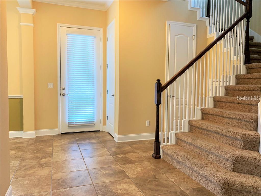 An entryway features tile flooring, a glass-paneled door, and a carpeted staircase with a railing — 8650 TAVISTOCK LAKES BOULEVARD, ORLANDO, FL
