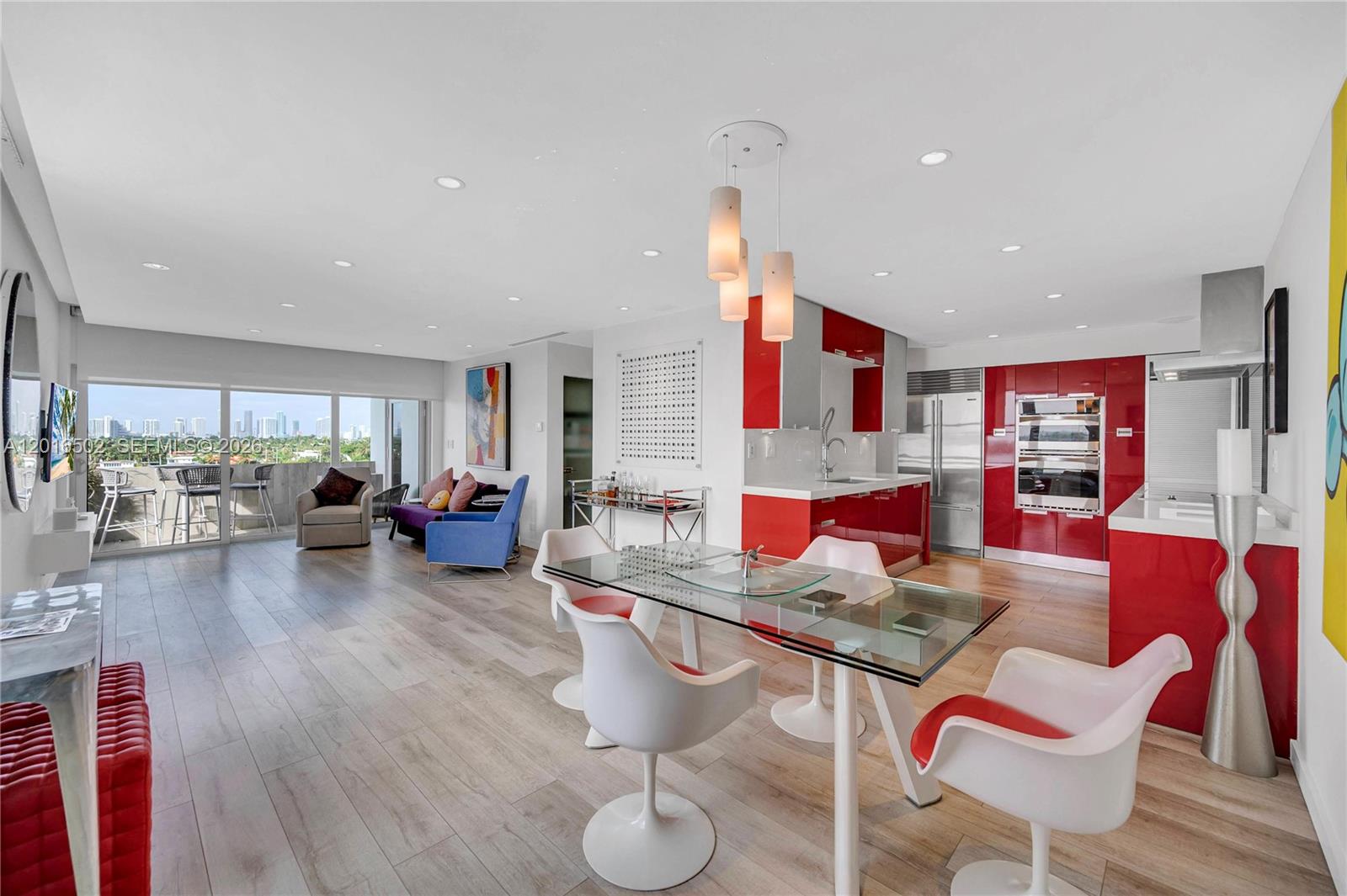 An open-concept living and dining area features red kitchen cabinets and a glass dining table — 3 Island Ave # 08I, Miami Beach FL 33139, MIAMI BEACH, FL