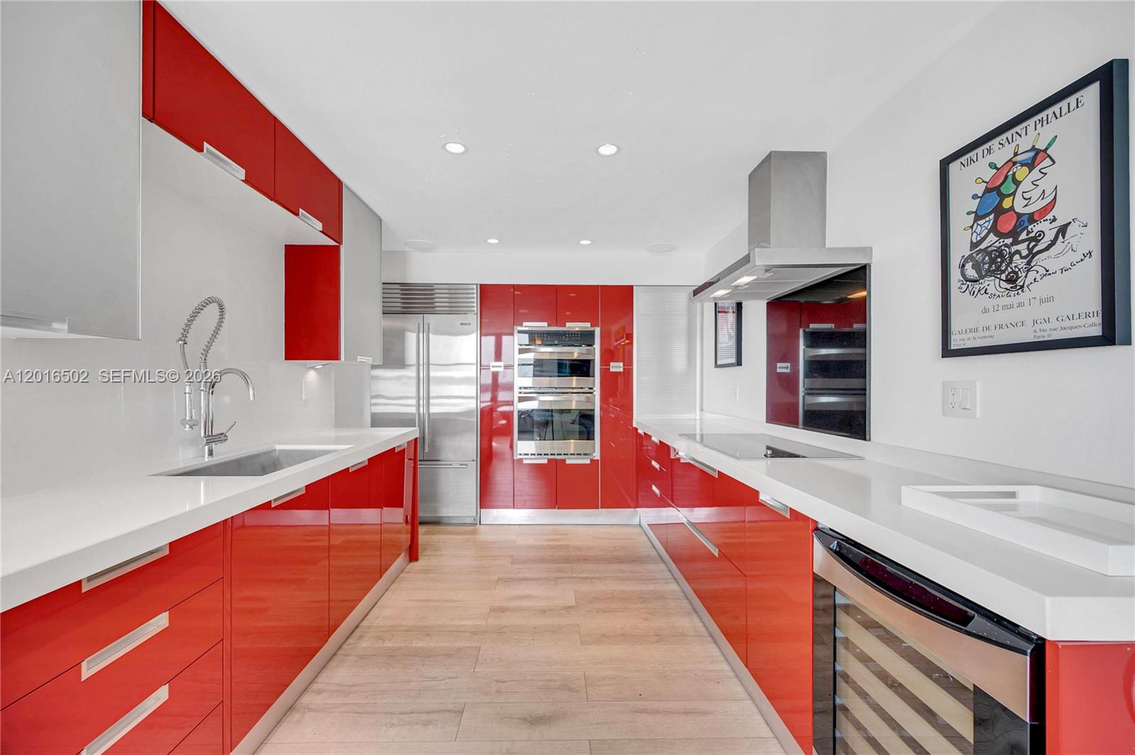 A modern kitchen features glossy red cabinetry, white countertops, and stainless steel appliances — 3 Island Ave # 08I, Miami Beach FL 33139, MIAMI BEACH, FL