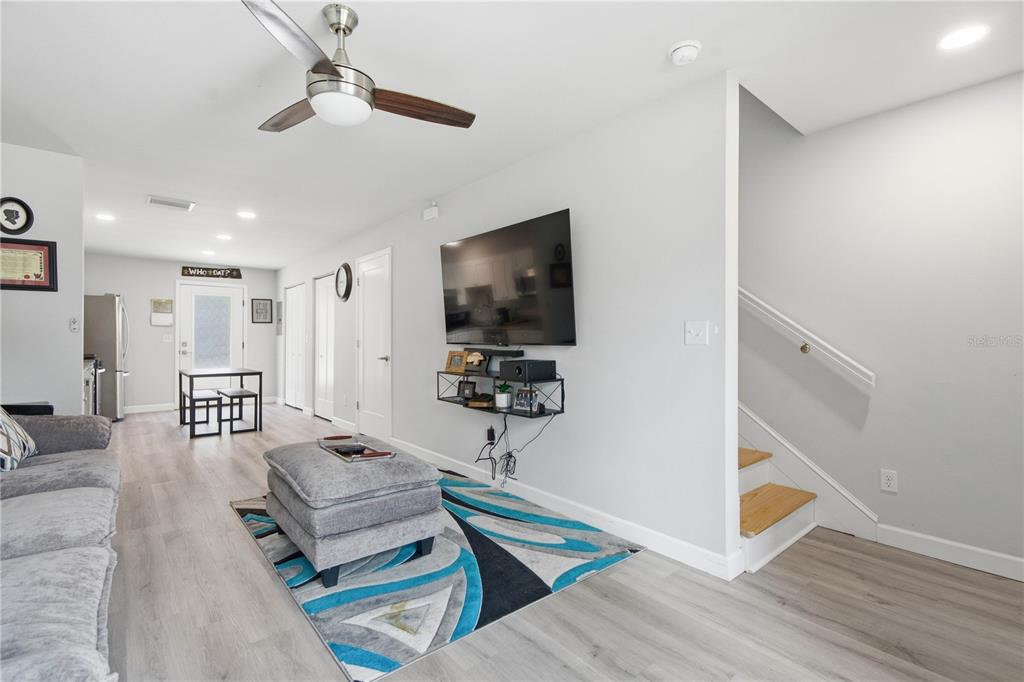 A living room features light wood flooring, a ceiling fan, a wall-mounted television, and stairs — 5729 75TH TERRACE N, PINELLAS PARK, FL