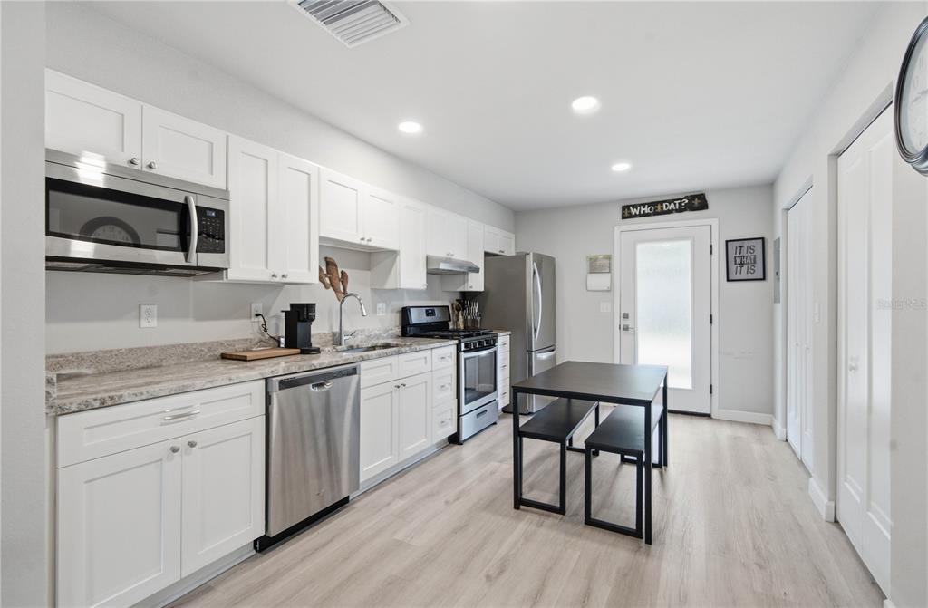 A modern kitchen features white cabinets, stainless steel appliances, light wood flooring, and a dining table — 5729 75TH TERRACE N, PINELLAS PARK, FL