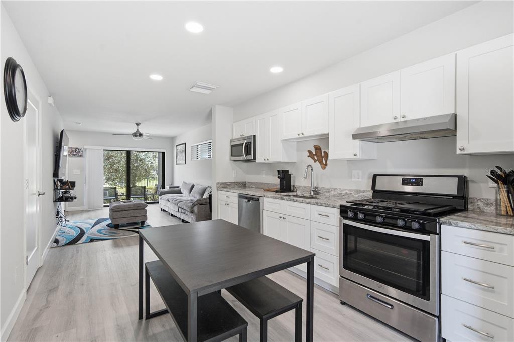 A kitchen with white cabinets and stainless steel appliances opens into a living area — 5729 75TH TERRACE N, PINELLAS PARK, FL