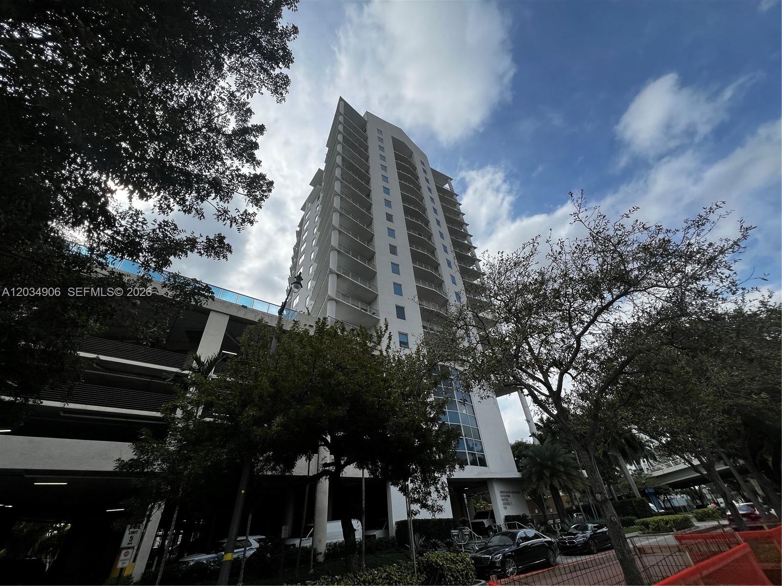 A tall residential high-rise building stands next to a parking garage under a cloudy sky — 10 SW South River Dr # 812, Miami FL 33130, MIAMI, FL