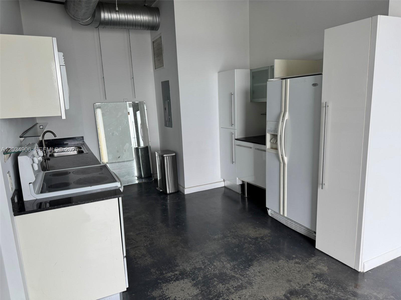 A kitchen features white cabinets, black countertops, a side-by-side refrigerator, and dark concrete flooring — 10 SW South River Dr # 812, Miami FL 33130, MIAMI, FL