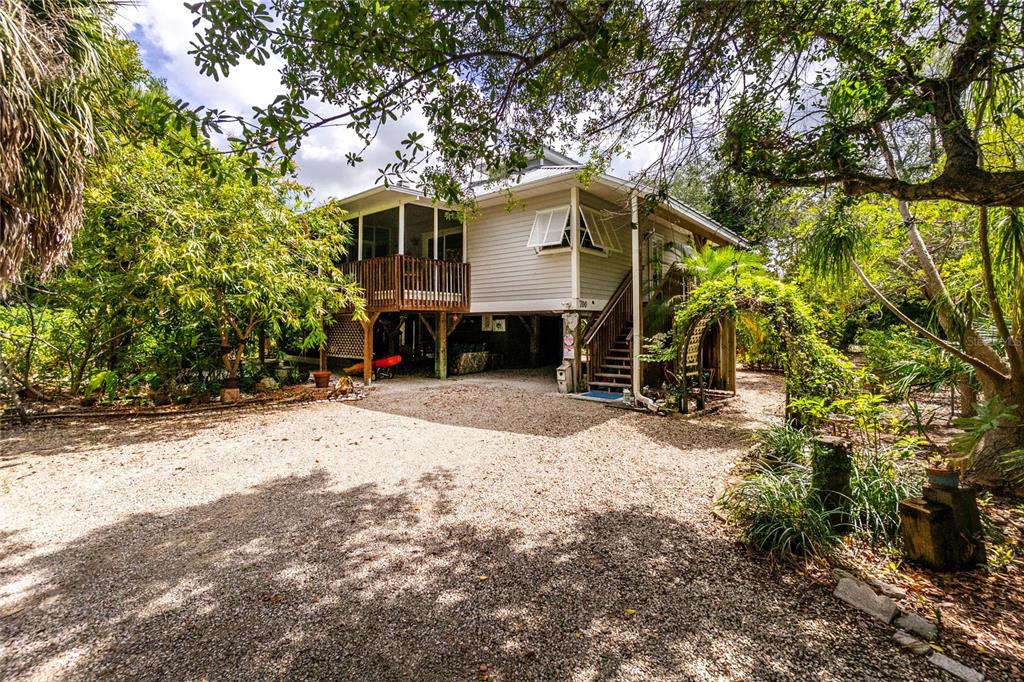 A stilt house with a gravel driveway, wooden deck, and surrounding lush tropical trees — 700 YALE STREET, ENGLEWOOD, FL