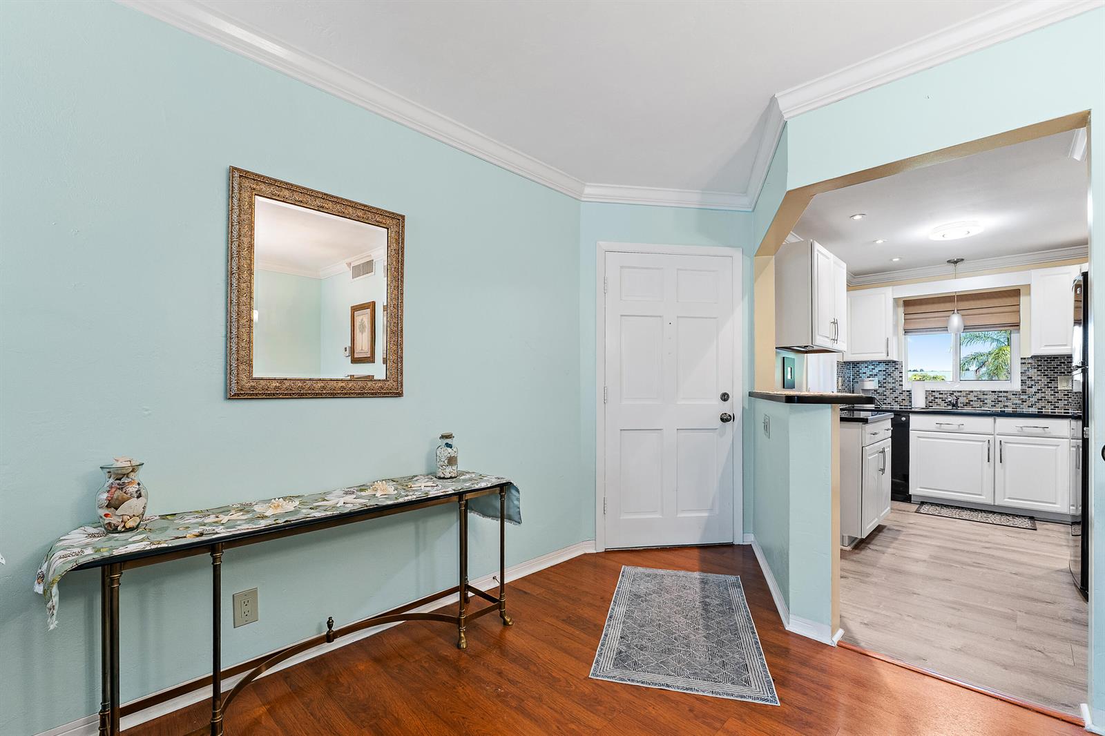 An entryway with light blue walls, wood flooring, a console table, and a kitchen view — 4 Westwood Avenue # 204, Jupiter FL 33469, JUPITER, FL