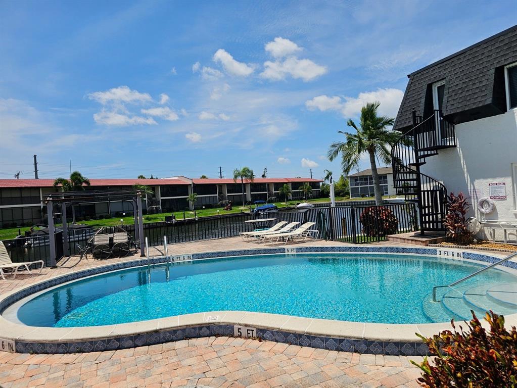A swimming pool with a brick deck sits beside a building with a spiral staircase — 4722 SE 1ST PLACE UNIT 5, CAPE CORAL, FL