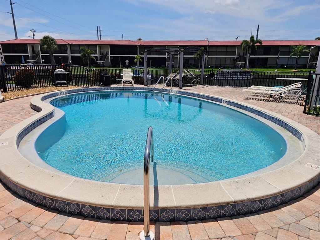 A kidney-shaped swimming pool with a metal handrail sits on a brick paver patio — 4722 SE 1ST PLACE UNIT 5, CAPE CORAL, FL