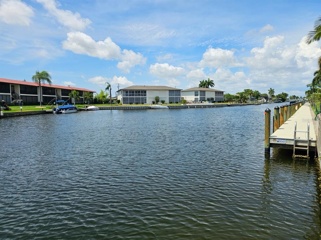 A canal view featuring a wooden dock, multi-story apartment buildings, and boats under a sky — 4722 SE 1ST PLACE UNIT 5, CAPE CORAL, FL